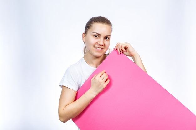 Una niña con una camiseta blanca sostiene una gran hoja de pancarta rosa en blanco en sus manos.