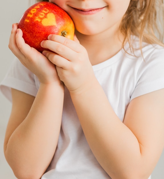 Una niña con una camiseta blanca sostiene una manzana en sus manos con la inscripción Te amo. Foto vertical