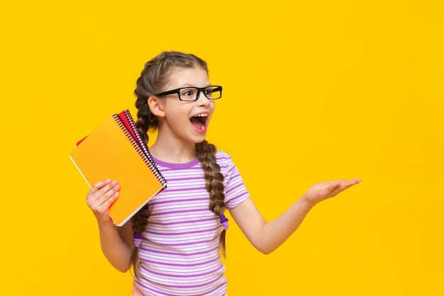Una niña con una camiseta a rayas señala hacia un lado el anuncio y sonríe Una niña con cuadernos en un fondo aislado