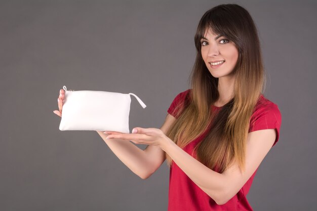 Una niña con una camiseta roja con una bolsa de cosméticos blanca.