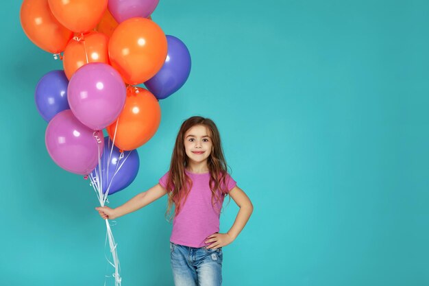 Niña en camiseta rosa posando con globos de aire de colores brillantes