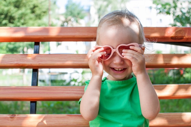 Foto niña con una camiseta verde y gafas de sol rosas en forma de corazón camina en el parque en verano