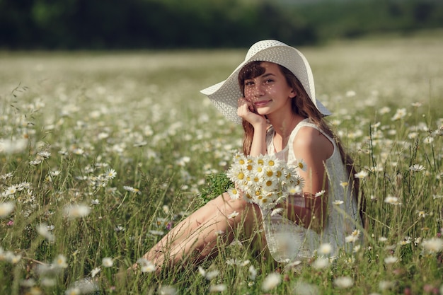 Niña en un campo de flores de margarita. La muchacha adolescente con sombrero y vestido disfruta de la primavera en el campo de margaritas. El concepto y la idea de una infancia feliz.