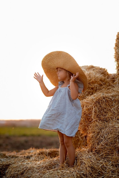 Niña en un campo con rollos de heno al atardecer Paisaje de un campo con montones de heno al atardecer Una niña con un vestido azul se encuentra en medio de un prado Armonía y amor por la naturaleza