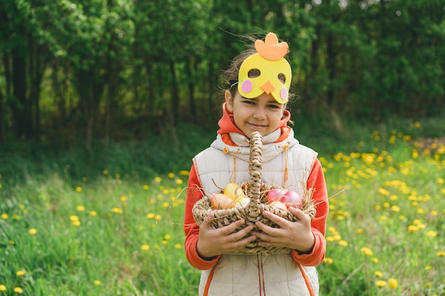 Niña con canasta de huevos y con una máscara de pollo en la caza de huevos de Pascua