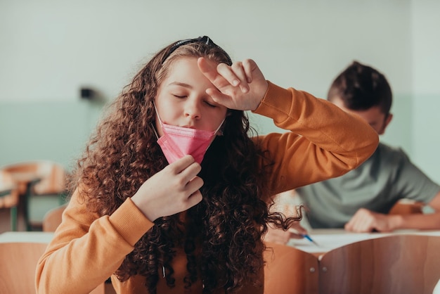 Niña cansada sentada en la escuela con una máscara en la cara para protegerse contra la pandemia del coronavirus Nueva educación normal durante la pandemia de Covid19 Enfoque selectivo Foto de alta calidad