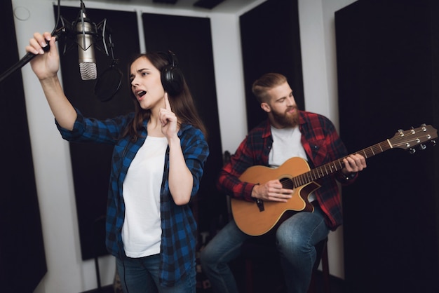 La niña canta mientras el chico toca la guitarra.