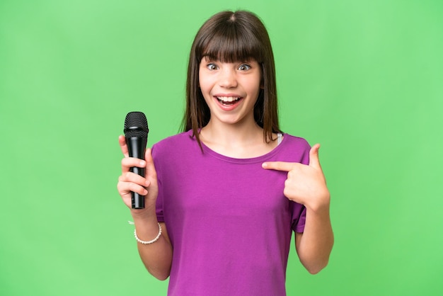 Niña cantante recogiendo un micrófono sobre un fondo aislado con expresión facial sorpresa