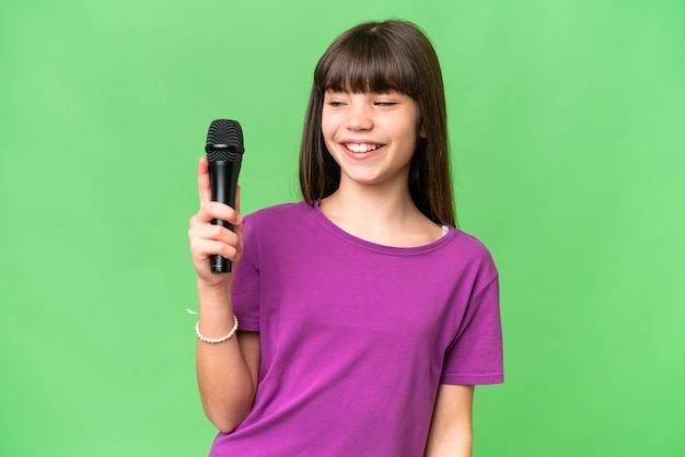 Niña cantante recogiendo un micrófono sobre un fondo aislado con expresión feliz