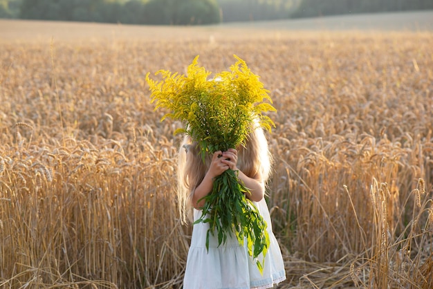 Una niña con la cara escondida detrás de un ramo de flores en un campo El concepto de despersonalización