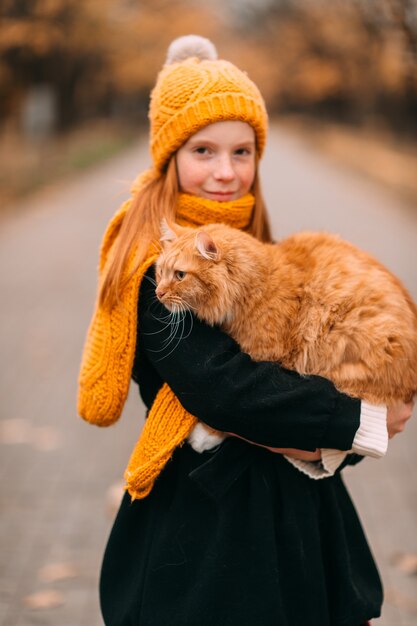 Niña con cara de pecas sosteniendo su gato en el parque de otoño.