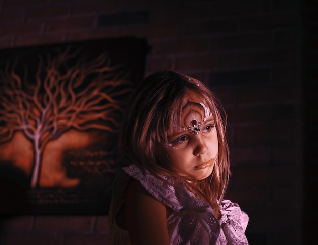 Foto niña con la cara pintada mirando hacia la pared