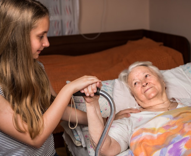 Niña cariñosa sosteniendo las manos de la anciana en la cama en casa