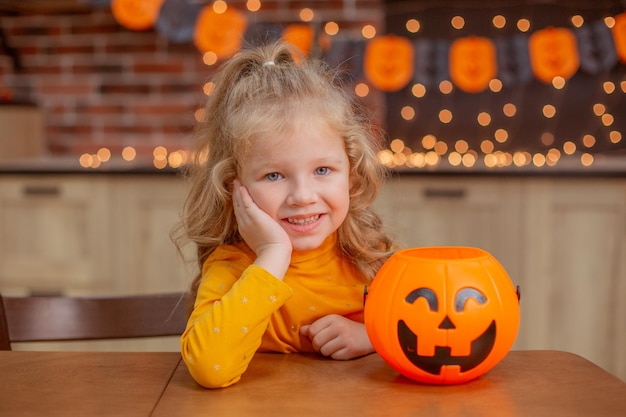 Niña en casa en la cocina en la mesa con una calabaza para halloween