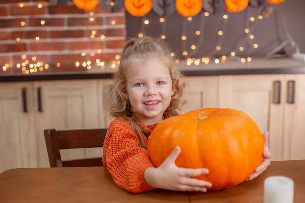 Niña en casa en la cocina en la mesa con una calabaza para halloween