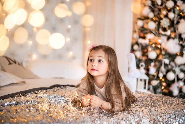 Una niña en casa en el fondo de un árbol de Navidad. Retrato en la cama