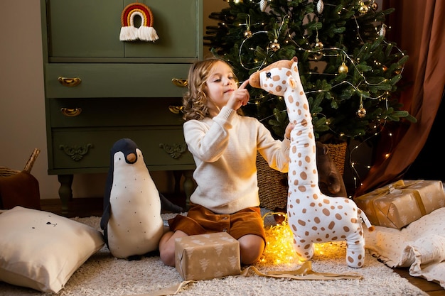 Niña en casa de Navidad cerca de la guirnalda festiva y abrazando sus lindos juguetes