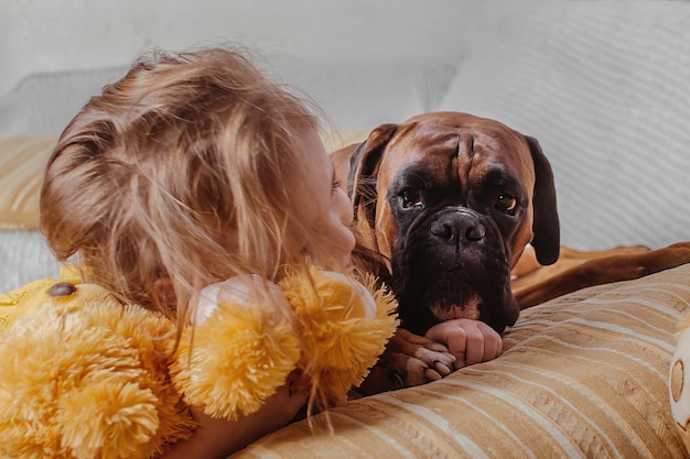 una niña en casa en el sofá juega con su boxeador alemán de raza de perro grande