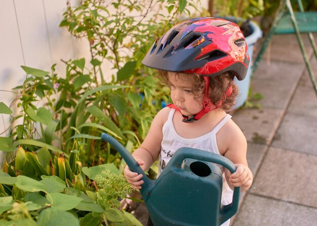 Foto una niña con casco de bicicleta está jugando en el patio trasero con plantas y regándolas