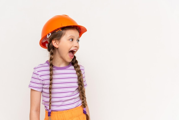 Una niña en un casco de construcción mira su anuncio en un fondo blanco aislado Copiar espacio El concepto de renovación en la habitación de los niños