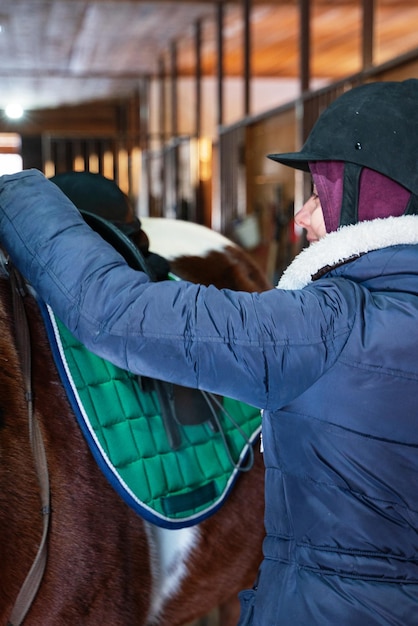 Una niña con casco de equitación ensilla su caballo