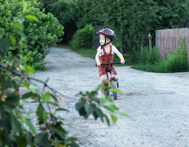 Foto niña con casco montando en bicicleta en el camino de entrada en el día de verano