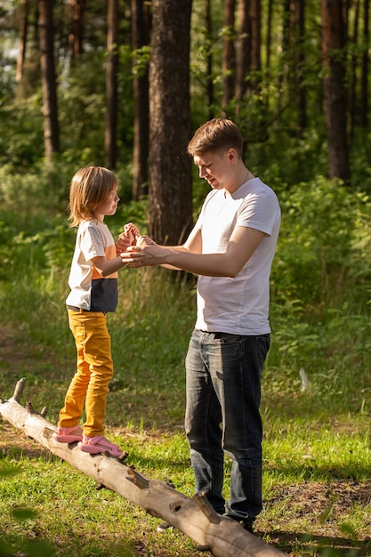 Niña caucásica de 6 años caminando sobre un tronco de la mano de papá. Padre e hija jugando juntos, riendo y divirtiéndose. Concepto de actividad familiar feliz