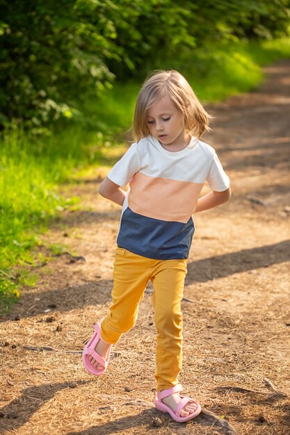 Niña caucásica de 6 años saltando sobre un camino en el bosque mirando a un lado