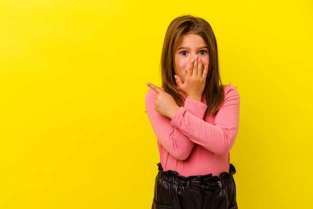 Niña caucásica aislada en amarillo apuntando hacia el lado