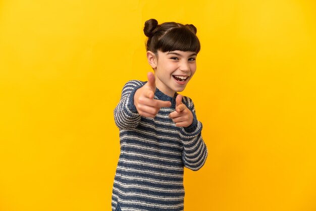 Niña caucásica aislada en amarillo sorprendido y apuntando al frente