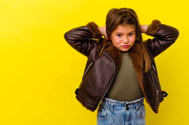 Foto niña caucásica aislada en amarillo tocando la parte posterior de la cabeza, pensando y tomando una decisión.