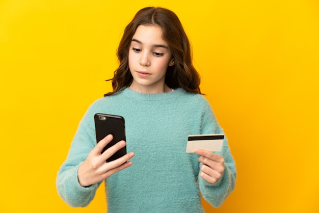 Niña caucásica aislada comprando con el móvil con tarjeta de crédito