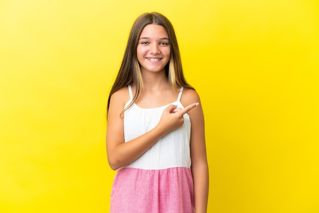 Niña caucásica aislada de fondo amarillo apuntando hacia un lado para presentar un producto