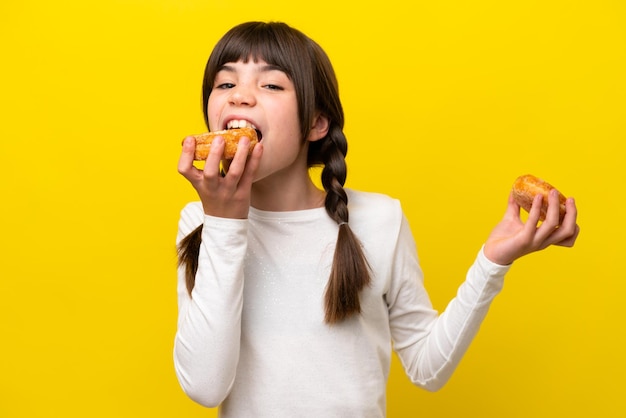 Niña caucásica aislada de fondo amarillo comiendo un donut