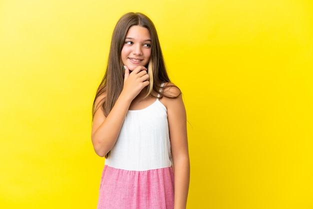 Niña caucásica aislada de fondo amarillo mirando hacia un lado y sonriendo