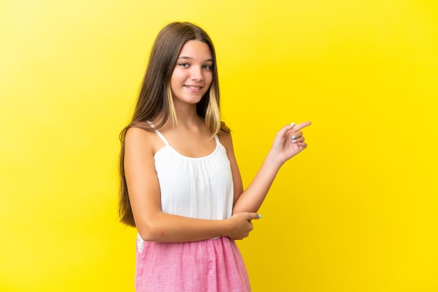 Niña caucásica aislada de fondo amarillo señalando con el dedo hacia un lado