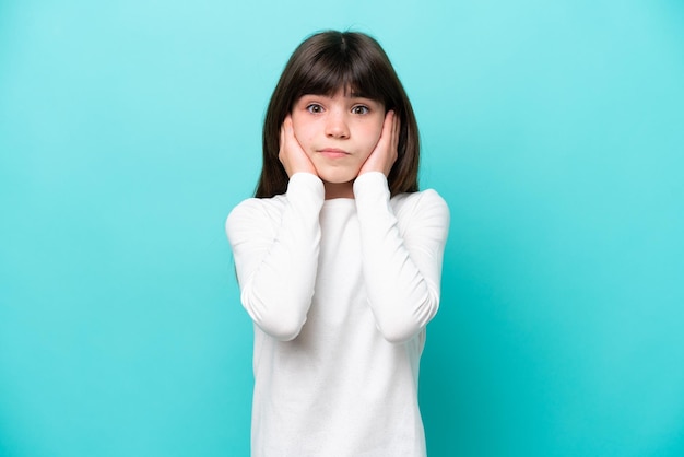 Niña caucásica aislada de fondo azul frustrada y cubriendo las orejas