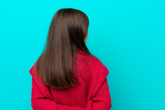 Niña caucásica aislada de fondo azul en posición trasera y mirando hacia atrás