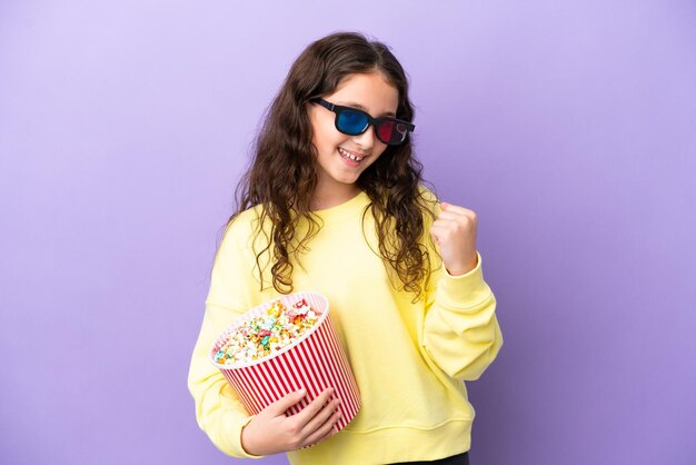 Niña caucásica aislada de fondo morado con gafas 3d y sosteniendo un gran cubo de palomitas de maíz