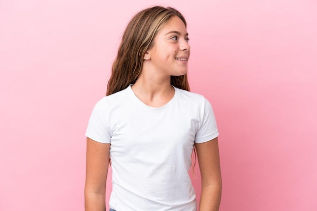 Niña caucásica aislada de fondo rosa mirando hacia un lado y sonriendo