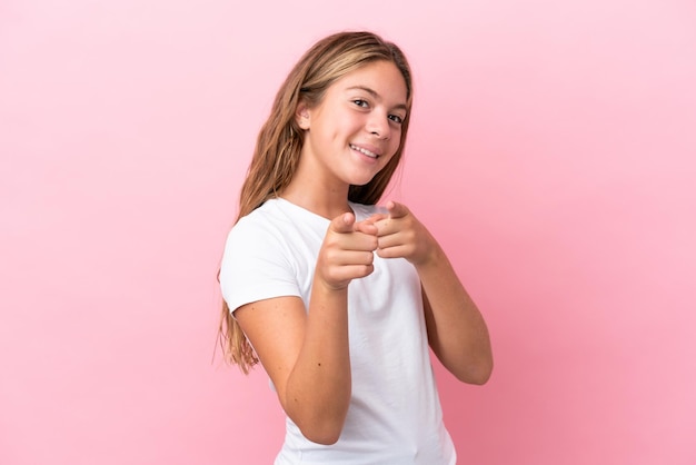 Niña caucásica aislada de fondo rosa sorprendida y apuntando al frente