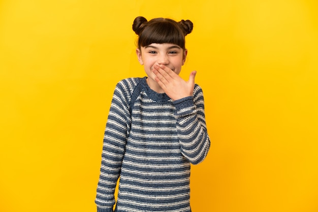 Niña caucásica aislada en la pared amarilla feliz y sonriente cubriendo la boca con la mano