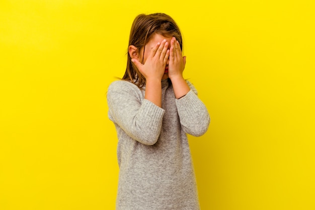 Niña caucásica aislada en la pared amarilla miedo cubrirse los ojos con las manos.