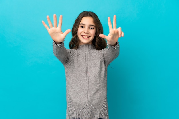 Niña caucásica aislada en la pared azul contando ocho con los dedos