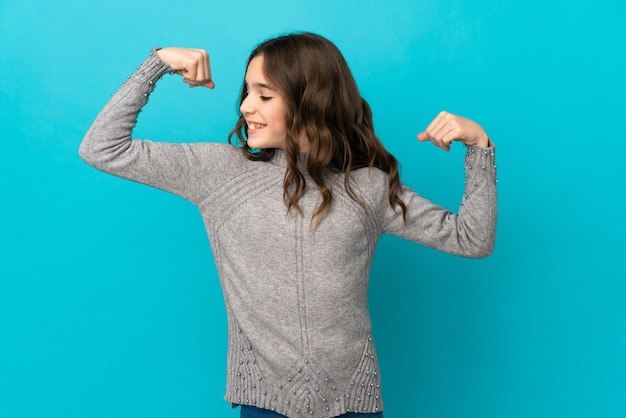 Foto niña caucásica aislada en la pared azul haciendo gesto fuerte