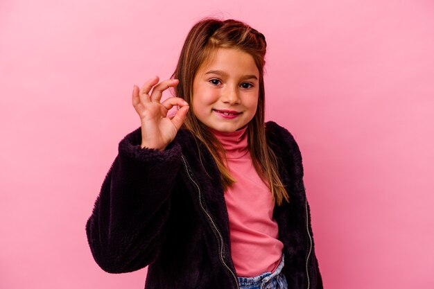 Niña caucásica aislada en rosa alegre y confiado mostrando gesto ok.