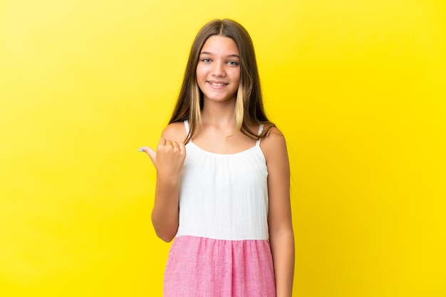 Niña caucásica aislada sobre fondo amarillo apuntando hacia el lado para presentar un producto