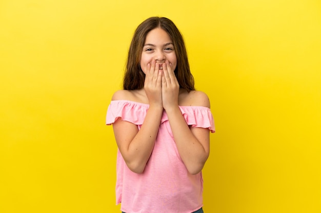 Niña caucásica aislada sobre fondo amarillo feliz y sonriente cubriendo la boca con las manos