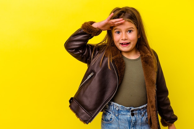 Niña caucásica aislada sobre fondo amarillo grita fuerte, mantiene los ojos abiertos y las manos tensas.