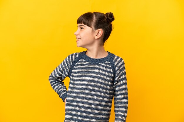 Niña caucásica aislada sobre fondo amarillo mirando hacia un lado y sonriendo